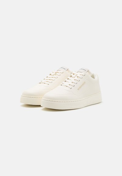 Sneakers bianche con una finitura liscia, punta rotonda, suola piatta e design con lacci. Perforazioni sottili e marchio sul lato.