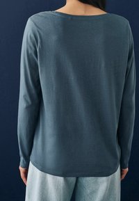 Langarmtop in donkerblauwe stof met een ronde hals, zachte textuur en een relaxte pasvorm, gecombineerd met lichte denimspijkerbroeken.