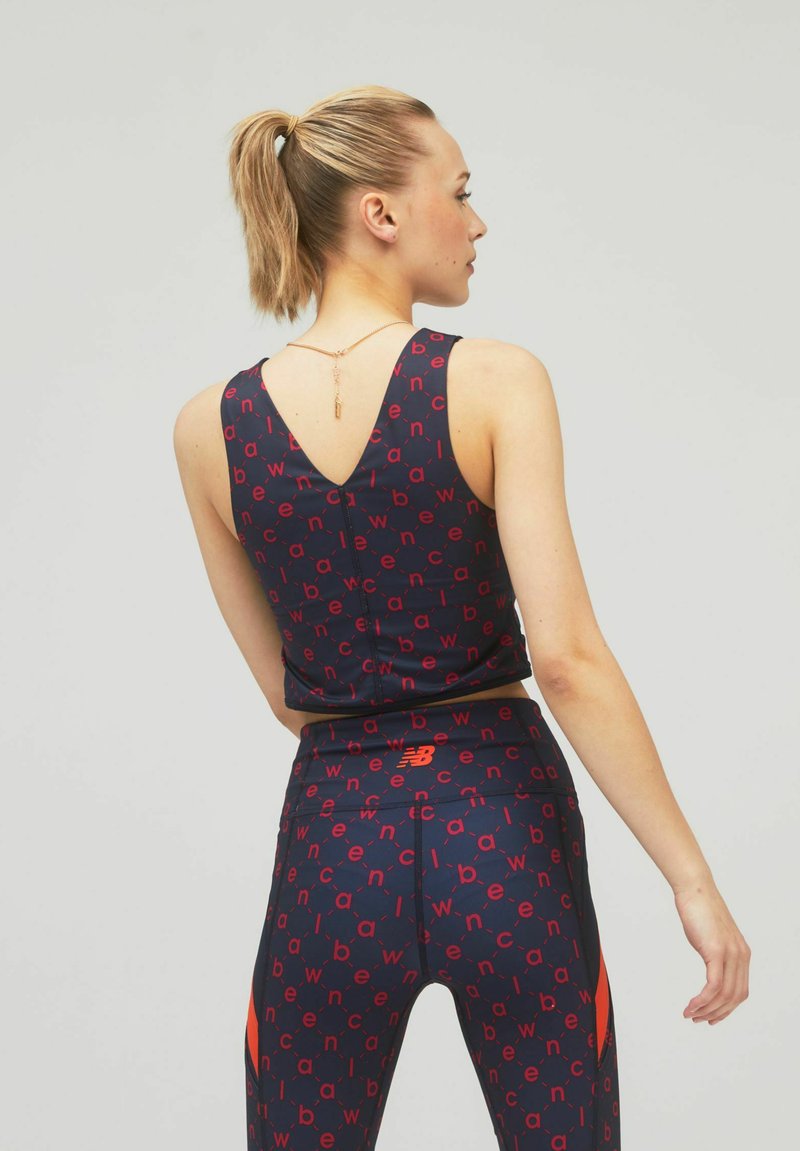 Crop top sportivo blu navale e leggings con motivi testuali rossi. Presenta un design con schiena a V, una silhouette aderente e accenti arancioni sui leggings.