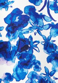 Tyg med blommönster i blå nyanser på en vit bakgrund, med en texturerad, vävd finish och varierande blomformer och storlekar.