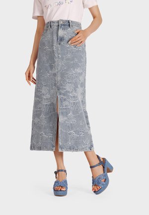 Gonna in denim con un design di mezza lunghezza, dotata di uno spacco frontale e intricate fantasie bianche. Abbinata a sandali con tacco intrecciati blu.