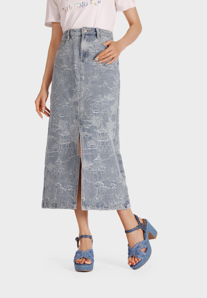 Gonna in denim con un design di mezza lunghezza, dotata di uno spacco frontale e intricate fantasie bianche. Abbinata a sandali con tacco intrecciati blu.