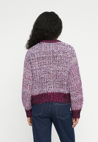 Pulôver de malha em tons de rosa e roxo, com um padrão texturizado, punhos canelados e um design cropped. Usado sobre jeans azuis.