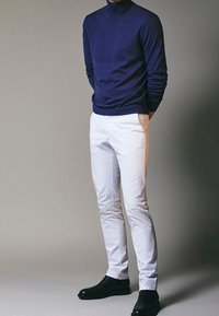 Maglione a collo alto di colore navy, pantaloni bianchi slim-fit e stivali neri alla caviglia. Il maglione presenta un tessuto a maglia strutturato; i pantaloni sono lisci e tagliati su misura.