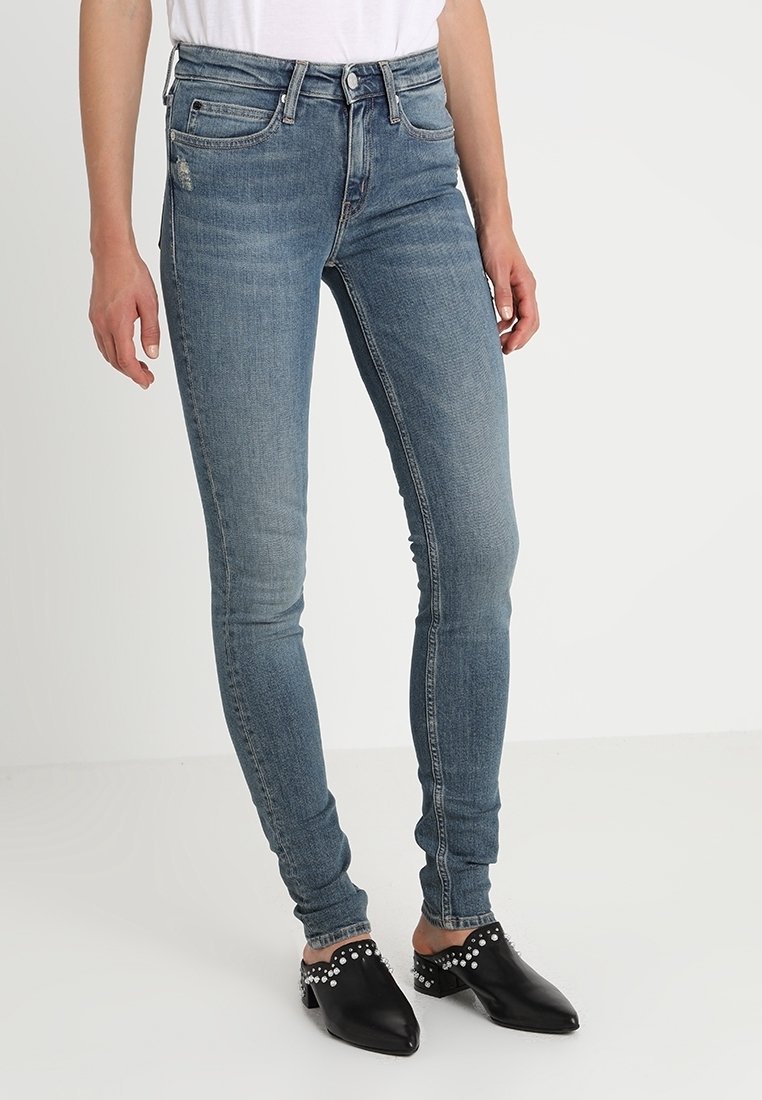 Hög midja blå skinny jeans i medeltvätt med en slät yta. Har framfickor och minimal slitage. Svarta nitar mules används.