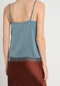 Camisole en satin bleu doux avec bretelles spaghetti réglables, ornée d'une délicate bordure en dentelle à l'ourlet, associée à une jupe en satin marron.