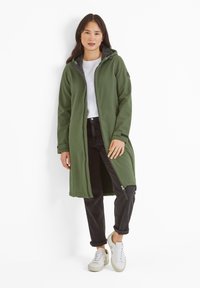 Green long coat with a hood, front zipper, and two side pockets, paired with a white shirt, black pants, and white sneakers.