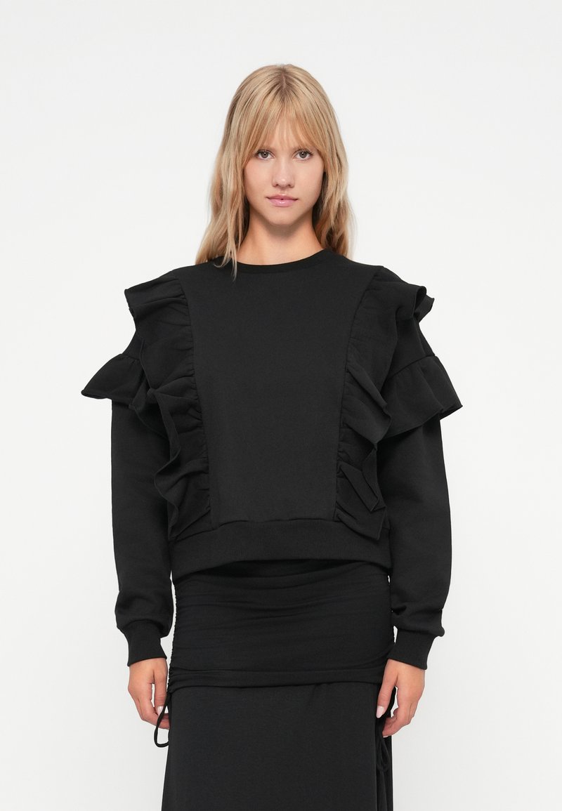 Hanorac negru cu accente volanate proeminente pe umeri și un design ajustat. Fabricat dintr-un material moale cu o textură mată.