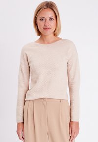 Hellbeige, strukturiertes Sweatshirt mit rundem Halsausschnitt und langen Ärmeln, kombiniert mit beigefarbenen Hosen, die über eine Frontknopfdetaillierung verfügen.