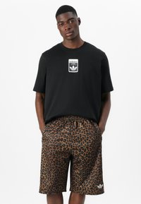Black cotton t-shirt with Adidas logo on the chest; brown leopard print shorts with an elastic waistband and side pockets.