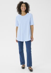 T-shirt azzurro chiaro a maniche corte, con scollatura tonda e vestibilità ampia, abbinato a jeans blu scuro e scarpe nere basse.