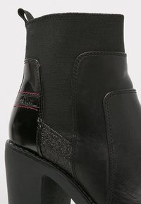 Bottines noires avec une combinaison de cuir lisse et de textile élastique, ornées d'un panneau accent pailleté et d'un talon block haut.
