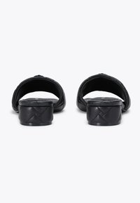 Sandali in pelle nera con apertura sul retro, texture trapuntata e tacco basso. Presentano una finitura liscia e dettagli di cucitura discreti.