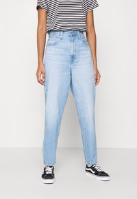 Ljusblå denim jeans med hög midja och avslappnad passform, något avsmalnande vid anklarna, i kombination med en svart och vit randig T-shirt och svarta sneakers.