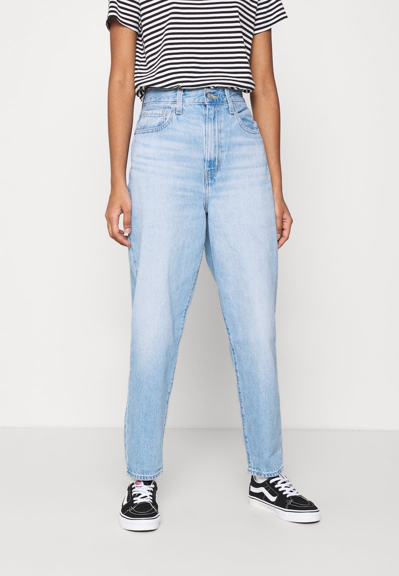 Ljusblå denim jeans med hög midja och avslappnad passform, något avsmalnande vid anklarna, i kombination med en svart och vit randig T-shirt och svarta sneakers.