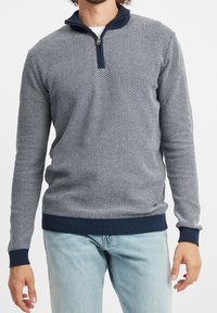 Pull léger zippé de couleur bleu marine avec un motif texturé, des poignets et un ourlet côtelés ; fabriqué en tissu tricoté doux, léger et ajusté.