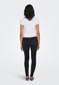 White ribbed short-sleeve top with ruffled edges, paired with fitted black jeans and brown flats. Back view, plain background.