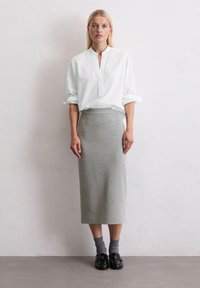 Bílá košile s límečkem, šedá midi sukně z úpletu a černé boty. Hladká tkanina, volný střih a minimalistický design. Sukně do poloviny lýtek.