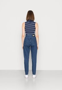 TOP sem mangas às riscas azul-marinho e brancas, calças de denim azul de cintura alta com bolsos traseiros e ténis brancos, vistas por trás.