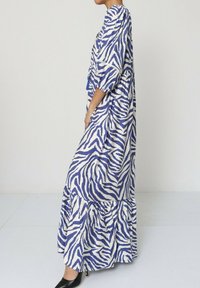 Robe maxi longue à imprimé zèbre bleu et blanc avec des manches courtes, un ourlet à volants superposés et une coupe décontractée. Texture lisse et tissu léger.