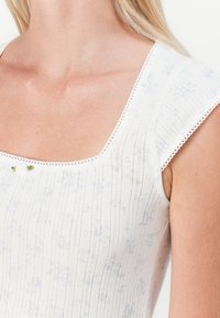 Bijela majica s kvadratnim izrezom, teksturirana tkanina koja sadrži vertikalne pruge, male cvjetne uzorke u plavoj boji i dekorativnu čipkastu oblogu na rukavima.