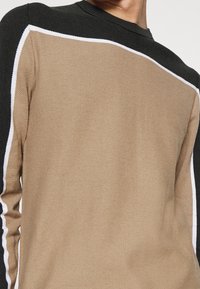 Maglione a maglia con corpo color sabbia, maniche nere e dettagli bianchi lungo la cucitura della spalla. Tessuto texturizzato con design a girocollo.