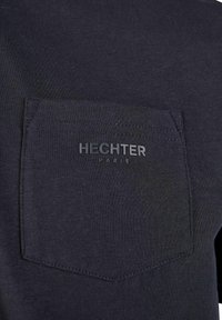 Donkerblauwe T-shirt met een gestructureerde stof en een opgestikte zak. De voorkant is eenvoudig, met "HECHTER" en "PARIS" in reliëf op de zak.