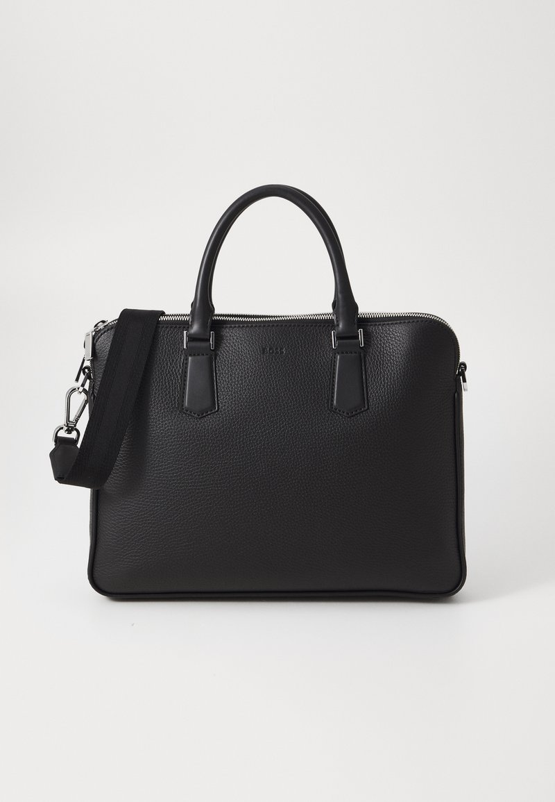Sac en cuir noir avec surface texturée, deux poignées et une bandoulière amovible. Il présente des fermetures éclair en argent et des éléments de design minimalistes.