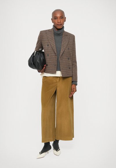 Blazer de doble botonadura en marrón de cuadritos, cuello alto gris, camisa crema, pantalones de pana anchos mostaza, bolso negro y zapatos de punta bicolor.