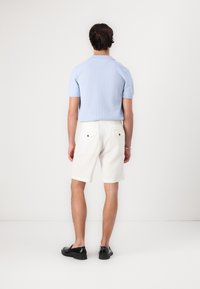 Polo shirt tricotat de culoare bleu deschis, pantaloni scurți albi cu talie elastică și buzunare la spate, asortați cu pantofi negri. Design simplu și casual.