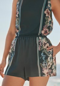 Mono corto con estampado floral en verde oscuro, que presenta un corte holgado, cintura elástica, bolsillos laterales y acentos de rayas verticales.