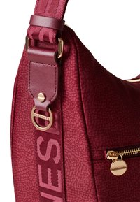 Burgunderfarbene Schultertasche mit strukturiertem Finish, goldenen Hardware-Akzenten und einem gemusterten Trageriemen. Verfügt über eine Reißverschlusstasche und ein Logo-Detail.