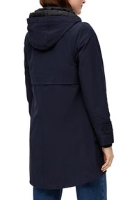 Marineblauwe waterdichte jas met een gebogen zwarte capuchon, een middellange stijl, zichtbare naden en knoopsluitingen aan de mouwen. Bevat een rugpand.