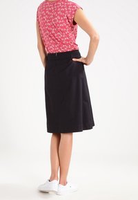 Sort A-line nederdel med en glat overflade. Kombineret med en rød blomstret bluse og hvide sneakers. Bagfra vises detaljer ved taljen.