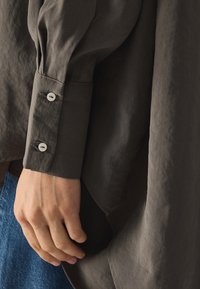 Camicia a maniche lunghe in tessuto grigio scuro con una finitura texture, caratterizzata da polsini con bottone e una vestibilità rilassata che scivola morbida.