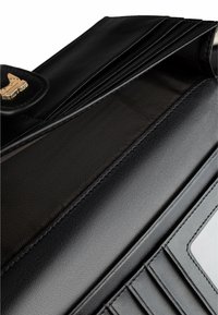 Wnętrze czarnej skórzanej torby o gładkiej fakturze, złotym okuciu i wieloma przegródkami na karty wyłożonymi paskowanym materiałem.