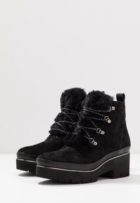 Stivali alla caviglia in suede nero con una fascia in pelliccia testurizzata, lacci in catena argentata e una suola platform nera spessa. Accentuati con dettagli metallici.