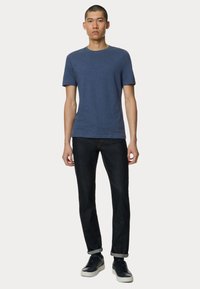 Námořnická modrá tričko s kulatým výstřihem v kombinaci s tmavými džíny, s ohrnutými manžetami a neformálními černými teniskami s bílými podrážkami.