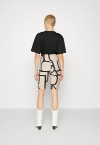 T-shirt noir surdimensionné, leggings marron avec de grands motifs noirs, et bottes de cowboy blanches. Texture lisse, coupe décontractée.