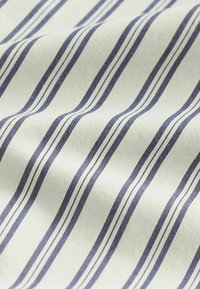 Bavlněná tkanina s alternujícími úzkými nápadně modrými a bílými pruhy, s hladkou texturou a mírně pomačkaným vzhledem.