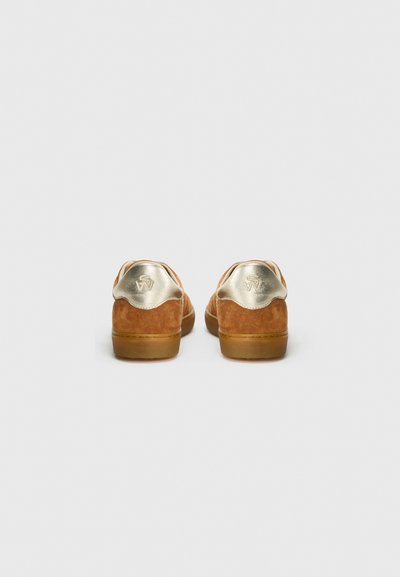 Sneakers in suede marrone con un elegante accento dorato sul tallone. Forma arrotondata, suola in gomma e un semplice logo impresso sul retro.