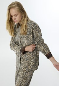 Een shirt met luipaardprint en bijpassende pantalons in beige en bruintinten, met geruite accenten op de boorden en de voorkruiken, gemaakt van zachte stof.