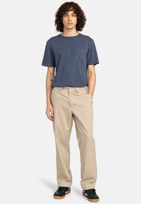 T-shirt en coton bleu marine avec une poche poitrine, associé à un pantalon chino droit beige et des baskets noires à semelle gomme.