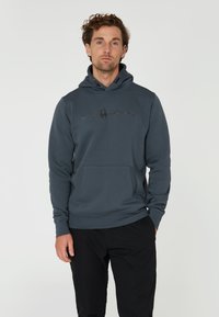 Mörkblå huvtröja i mjukt tyg, med en framficka och dragsko till huvudet. "SAIL RACING"-logotypen är tydligt synlig i svart.