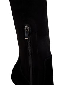 Bota de ante negra hasta la rodilla con cremallera lateral y textura suave, con un ajuste contorneado y mínimos acentos de hardware.