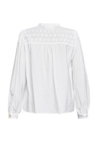 Hvid langærmet bluse med tekstureret stof, der har et broderie anglaise design på yoke og knappede manchetter.
