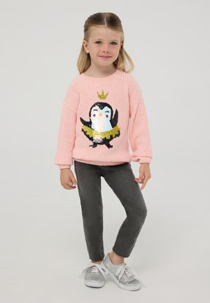 Różowy sweter z dzianiny z motywem pingwina, ozdobiony cekinami, w połączeniu z szarymi spodniami slim-fit i srebrnymi butami.