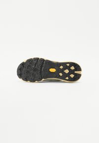 Semelle de sneaker avec une surface en caoutchouc noir, des motifs de bande de roulement multidirectionnels et un bord beige avec un logo Vibram.