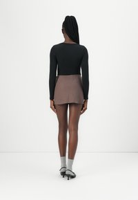 Fekete bordás hosszú ujjú felső barna mini szoknyával, ami textúrált mintával rendelkezik, szürke zoknikkal és fekete magassarkú cipőkkel kiegészítve.