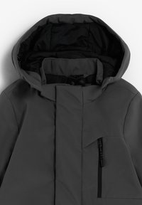 Chaqueta de invierno gris oscuro con capucha acolchada, cremallera frontal cubierta por una solapa y bolsillo en el pecho con cremallera.